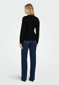 Melna pieguļošā džemperis ar garām piedurknēm un ribotām malām. Līdz ar to saskan tumši zili taisni bikses, kurām ir aizmugurējo kabatu izšuvuma detaļas.