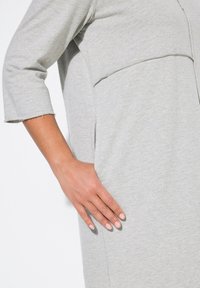 Robe-sweat grise avec une coupe décontractée, dotée d'une poche avant et de manches trois-quarts, fabriquée en tissu doux et texturé.