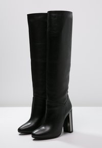 Knöchelhohe schwarze Lederstiefel mit spitzer Zehenpartie und blockigem Absatz, der mit einem glänzenden silbernen Akzent verziert ist. Geschmeidige Textur und figurschmeichelndes Design.