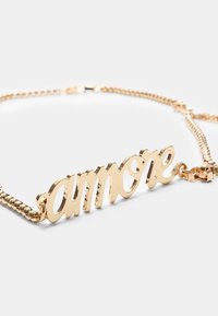 Collier en ton or avec un pendentif portant le mot "amore" en écriture cursive. La chaîne est texturée avec un design classique.