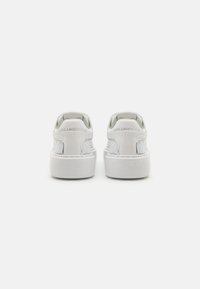 Sneaker bianche dal design elegante, con un pannello in tessuto testurizzato sul lato, suola piatta e logo impresso sul tallone.