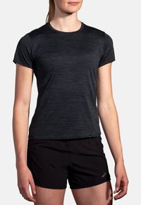Camisa deportiva corta negra con mangas cortas y un patrón texturizado jaspeado. Presenta un escote redondo y un logo sutil en el dobladillo.