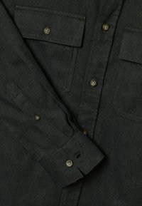 Donkergroen flanellen overhemd met twee borstzakken, bruine knopen en een zichtbare textuur. De manchetten zijn voorzien van een knoopsluiting en een inzetten detail.
