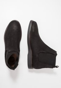 Bottines en suède noir avec des panneaux élastiques sur les côtés, bout rond, petit talon empilé et languette à l'arrière pour un enfilage facile.