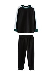 Haut noir à manches longues avec bandes blanches sur les côtés et poignets verts, associé à un pantalon noir à taille élastique avec chevilles retroussées.