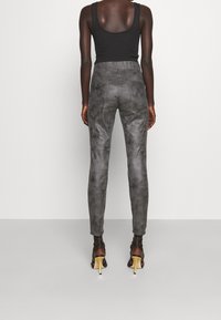 Svart linne bärs med grå, åtsittande byxor med en strukturerad, något fläckig yta, och högklackade skor med gula accenter.