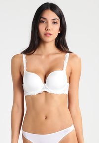 Soutien-gorge blanc rembourré avec des bordures en dentelle, bretelles ajustables et forme ronde. Texture lisse sans motifs ni éléments visibles.