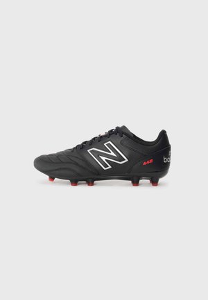 Black soccer cleat in synthetic material with white logo, red accents, textured upper, and multiple red studs on base for traction.