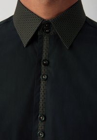 Camicia nera con un colletto a fantasia verde texturizzato, patta frontale con bottoni scuri e finitura del tessuto liscia.