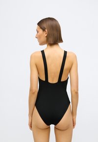 Fekete bordázott egyrészes fürdőruha széles pántokkal, nyitott hátkiképzéssel és magasra vágott lábszárakkal. Sima textúra és minimalista stílus.