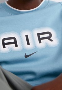 Ljust blå sweatshirt med fet "AIR"-text i svart med vita konturer, samt en liten svart Nike-logotyp ovanför nederkanten.