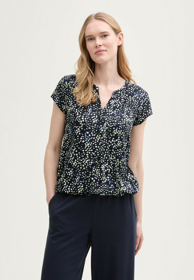 Blouse courte navy à manches courtes avec un décolleté en v, motif de points blancs, verts et bleus dispersés, coupe décontractée et détail plissé à l'avant.