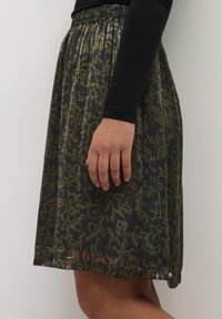 Jupe plissée en tissu noir transparent avec un motif floral vert. Elle possède une taille élastique et tombe juste au-dessus du genou.
