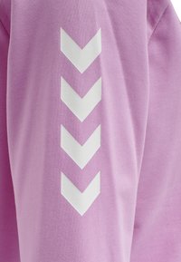 Lila tyg har en texturerad yta med ett vitt chevronmönster längs ärmen. Designen är modern och geometrisk.