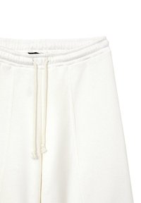 Pantaloni della tuta bianchi con cintura elastica e stringhe, cuciture laterali e un tessuto morbido e texturizzato. Nessun marchio o motivo visibile.