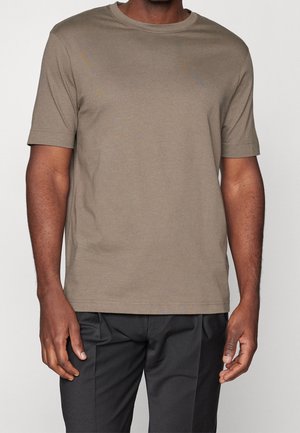 T-shirt kaki à manches courtes fabriqué dans un matériau doux et lisse ; doté d'un col rond et d'un ourlet droit. Porté avec un pantalon noir.