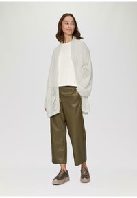 Leichtes Strick-Cardigan in Weiß, lockeres weißes Oberteil, olivgrüne, taillierte Hosen aus Kunstleder und braune Sneakers mit strukturierten Akzenten.