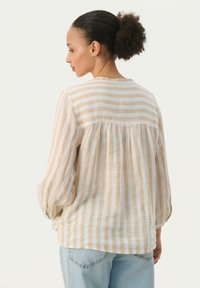 Lightweight, striped shirt in beige and cream, featuring long, puffed sleeves and a gathered back detail. Paired with denim jeans.