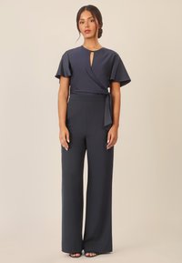 Marineblauw jumpsuit met korte vleugelmouwen, een keyhole halslijn, een ceintuur in de taille en een wijde broekspijpen ontwerp. Zachte stof en getailleerde pasvorm.