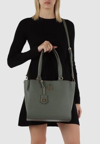 Borsa a tracolla verde in ecopelle con due manici superiori, tracolla staccabile, dettagli in hardware dorato e un'etichetta appesa. Finitura liscia al tatto.