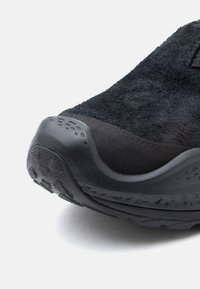 Musta urheilukenkä, jossa on tekstuurinen mokkanahkapinta, kumipohja ja muotoiltu varvaskuppi, jossa on pyöreitä kuvioita.