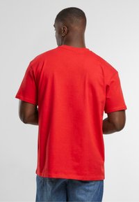 Rød kortærmet t-shirt lavet af bomuld. Lige skåret design med rund hals og en glat tekstur. Båret sammen med blå denim jeans.