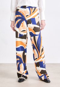 Wide-leg trousers made from a smooth, lightweight fabric feature a vibrant abstract pattern in orange, blue, brown, and cream tones.