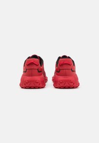 Paire de baskets Hugo rouges et noires vues de dos, avec semelles texturées et languettes de tirage au talon, sur fond blanc.