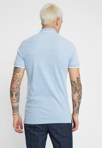 Lys blå, kortermet polo shirt med flat krage. Myk tekstur og rett snitt, med hvite detaljer ved kragen og ermene.