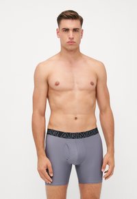 Graue Boxershorts mit einem schwarzen Bund, auf dem das "Under Armour" Logo zu sehen ist. Der Stoff wirkt glatt und enganliegend, ausgelegt für Komfort und Unterstützung.