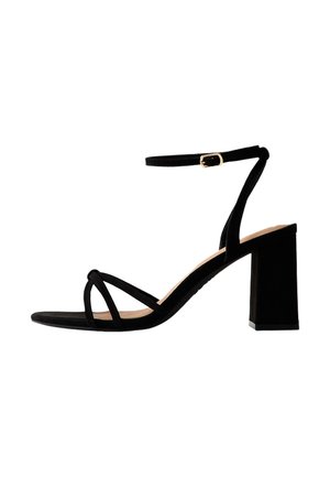 Czarna zamszowa sandałka na wysokim obcasie typu block, z cienkimi skrzyżowanymi paskami na palcach oraz paskiem wokół kostki z małą złotą klamrą.