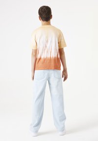 Camiseta de tie-dye en naranja y crema con efecto degradado, combinada con jeans holgados de color azul claro y zapatillas blancas.