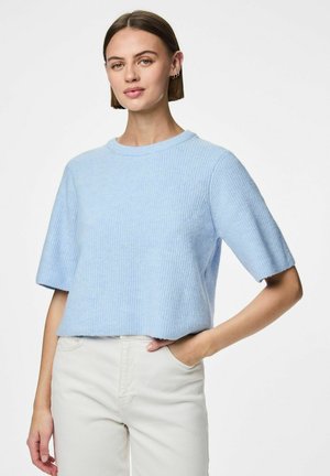 Helles blaues Strickoberteil, kurze Ärmel, geripptes Muster, runder Halsausschnitt, cropped Design, getragen mit weißen Hosen, Hände in den Taschen.