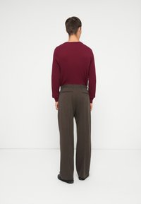Cămașă lungă maroniu, cu un model texturat, asociată cu pantaloni largi de culoare maro, care au două buzunare pe spate și o finisare netedă.