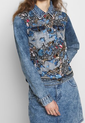 Jeansjacke mit floraler Paillettenstickerei über einem passenden Jeansrock, getragen von einer Person mit langen braunen Haaren.