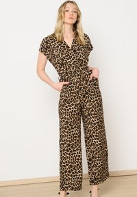 Mono de leopardo con mangas cortas, escote en forma de V y pantalones de pierna ancha. Presenta una cintura ceñida y bolsillos laterales. La tela es ligera.