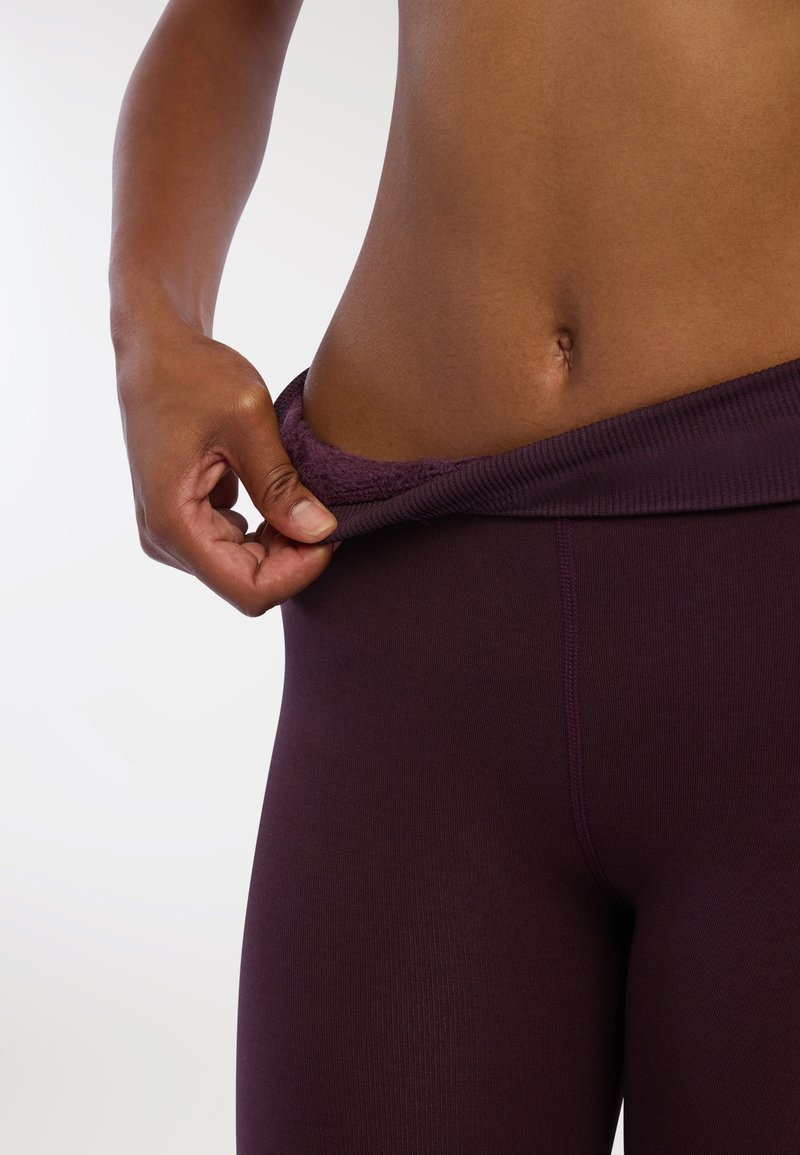 Fioletowe legginsy sportowe z teksturowanym pasem, lekko zdejmowane, eksponujące gładki materiał i dopasowany krój.
