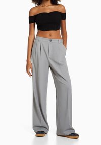 Černý off-shoulder krácený top v kombinaci se světle šedými širokými kalhotami, které mají sklady a boční kapsy, texturovanou látku a zapínání na knoflík.