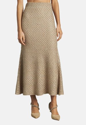 Falda maxi de punto en beige con un tejido texturizado, dobladillo acampanado y cinturilla ajustada, combinada con tacones nude decorados.