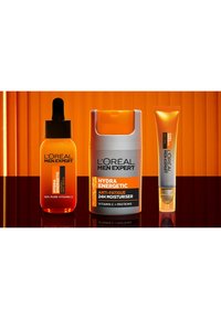 Trois produits de soin de la peau L'Oréal Men Expert : un flacon compte-gouttes avec un sérum orange, une crème hydratante grise avec des accents orange, et un tube argenté avec un embout à bille.