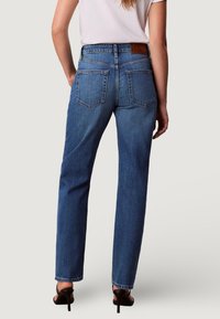 Jeans de mezclilla azul con pierna recta, cintura alta y un ligero efecto desgastado. Cuenta con dos bolsillos traseros y una etiqueta de cuero con el logo en la cintura.