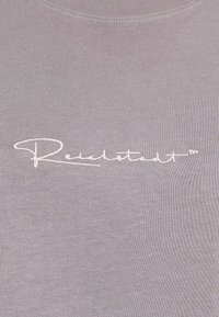 Lichtgrijze geribbelde t-shirt met een witte geborduurde logo op de voorkant. De stof is soepel met een aansluitend ontwerp en een ronde hals.