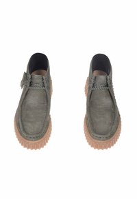 Scarpe in pelle grigia con forma arrotondata, superficie testurizzata, lacci grigi e una suola spessa in gomma marrone chiaro con scanalature.