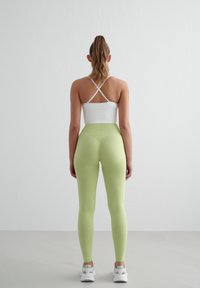 Haut de sport blanc avec des bretelles croisées, associé à des leggings vert clair. Les leggings ont une taille haute et une texture lisse.