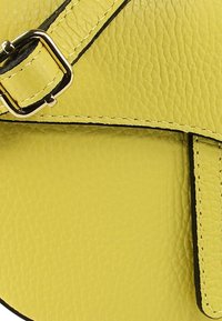 Gele leren tas met textuur, een zwarte accentnaad en een metalen gespdetail op de verstelbare riem.