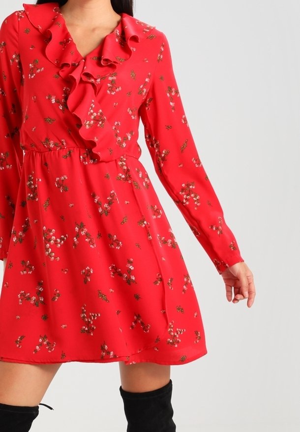 Robe longue rouge à fleurs à manches longues avec col en V volanté et taille cintrée, portée avec des bottes noires cuissardes.