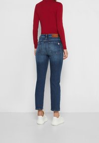 Jeans de tiro alto, de color azul oscuro, con corte recto, que cuentan con dos bolsillos traseros y un parche de cuero. Combinados con una parte superior ajustada de manga larga roja y zapatillas blancas.
