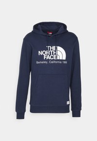 Sweat à capuche bleu marine avec poche avant, cordon de serrage et logo blanc "The North Face Berkeley, California 1966" sur la poitrine.
