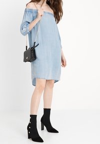 Světle modré džíny šaty s odhalenými rameny, volného střihu a s ohrnutými rukávy, doplněné černými semišovými kotníkovými botami s pozlacenými knoflíky.