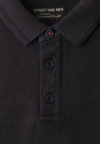 Polo noir texturé avec col côtelé, trois boutons noirs et étiquette "Street One Men" portant le slogan confort inégalé.